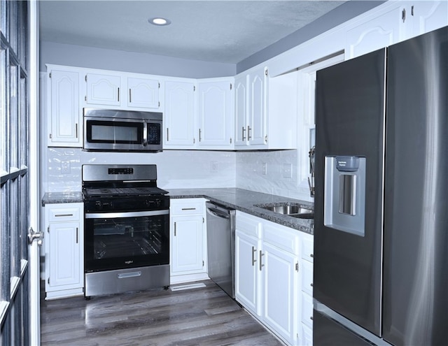 kitchen with white cabinetry, appliances with stainless steel finishes, dark stone counters, and dark hardwood / wood-style floors