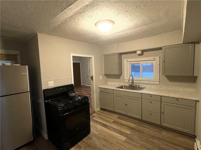 kitchen featuring sink, black range with gas stovetop, stainless steel fridge, a textured ceiling, and hardwood / wood-style flooring