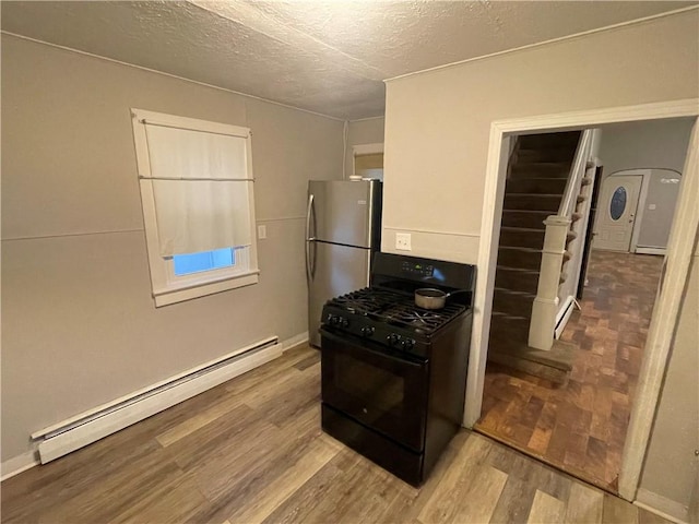 kitchen featuring black range with gas cooktop, a textured ceiling, a baseboard heating unit, light hardwood / wood-style floors, and stainless steel refrigerator