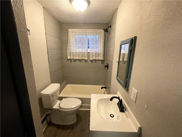 full bathroom featuring vanity, a textured ceiling, tiled shower / bath combo, hardwood / wood-style flooring, and toilet