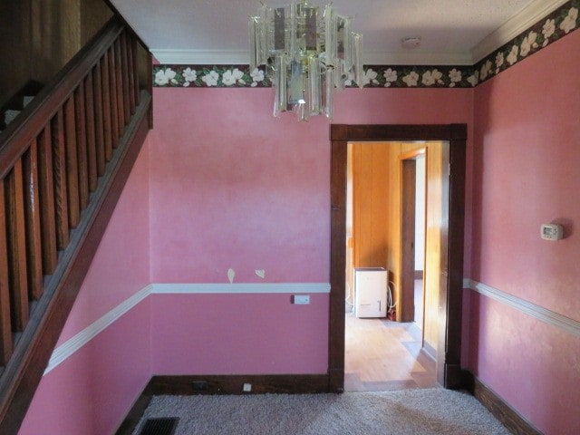 empty room with a chandelier, carpet, and ornamental molding