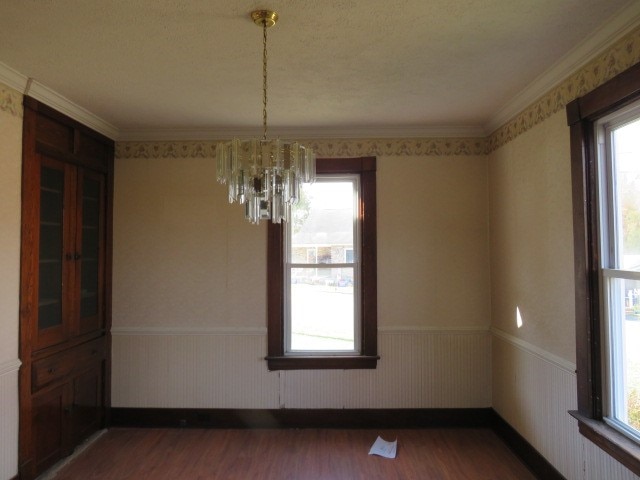 unfurnished dining area with wood-type flooring, wooden walls, a chandelier, and ornamental molding