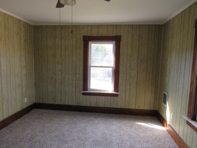 spare room featuring wooden walls, ceiling fan, and carpet floors