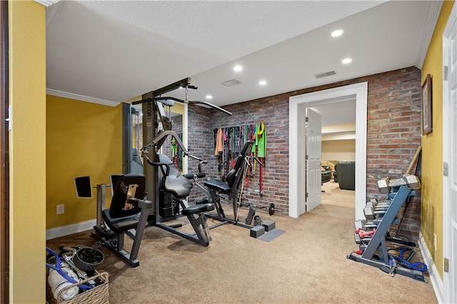 exercise room featuring a textured ceiling, light carpet, ornamental molding, and brick wall