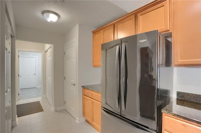 kitchen with stainless steel fridge, light tile patterned floors, dark stone counters, and a textured ceiling