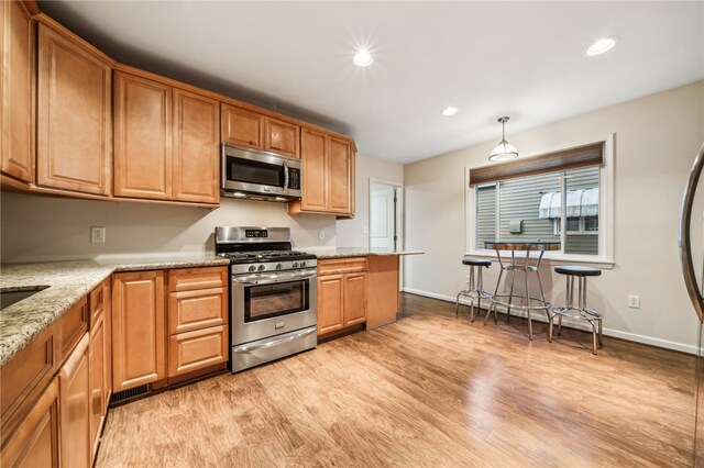 kitchen with stainless steel appliances, decorative light fixtures, light hardwood / wood-style floors, and light stone counters