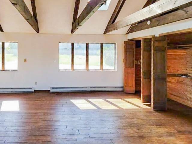 unfurnished living room featuring beam ceiling, hardwood / wood-style flooring, baseboard heating, plenty of natural light, and high vaulted ceiling