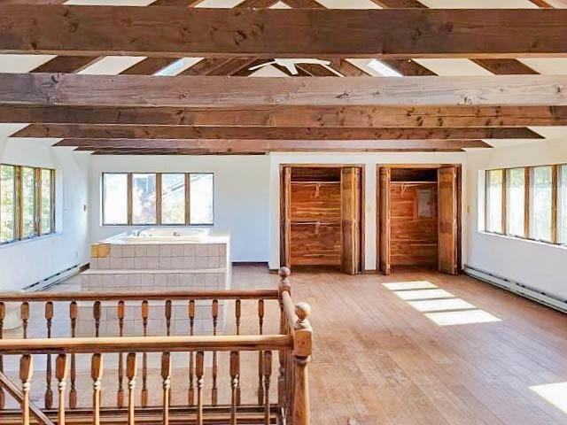 unfurnished bedroom with beam ceiling, a baseboard radiator, wood finished floors, and multiple closets