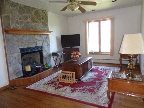 living room with a baseboard radiator, hardwood / wood-style floors, ceiling fan, and a fireplace