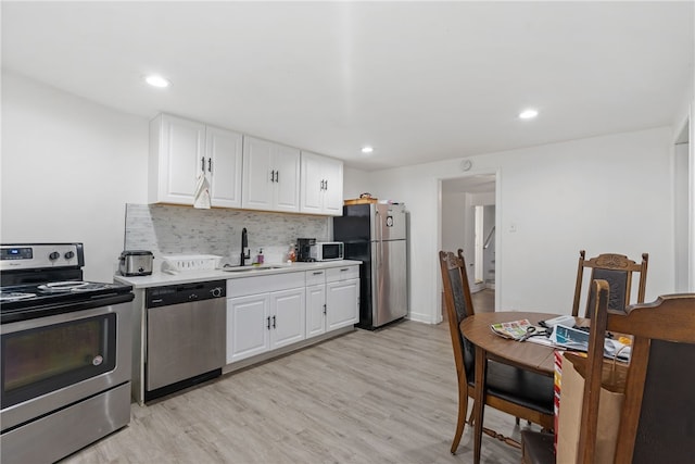 kitchen with light hardwood / wood-style floors, white cabinetry, sink, appliances with stainless steel finishes, and backsplash