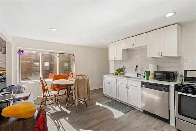 kitchen with white cabinetry, appliances with stainless steel finishes, decorative backsplash, sink, and light hardwood / wood-style floors