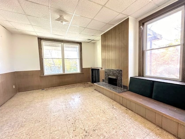 unfurnished living room featuring a paneled ceiling, wooden walls, and a fireplace