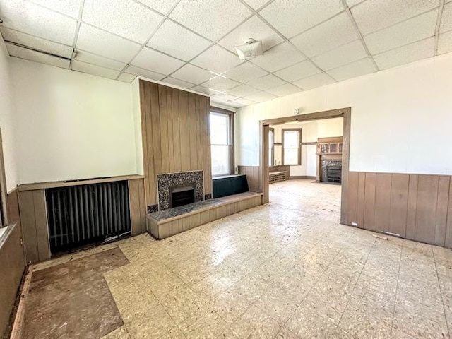 unfurnished living room featuring a drop ceiling, wooden walls, and a fireplace