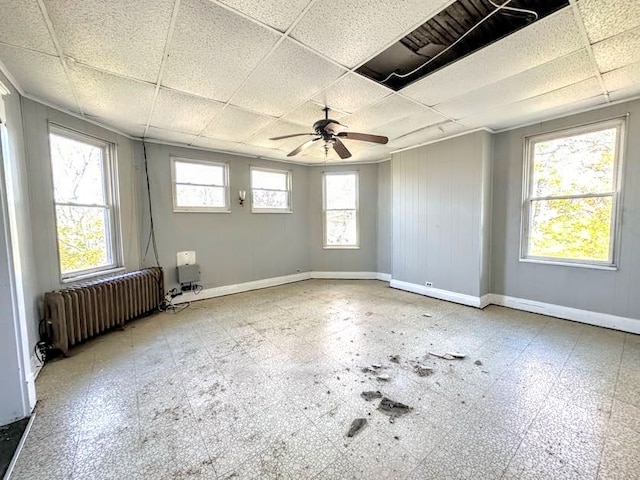 empty room featuring radiator, ceiling fan, and a drop ceiling