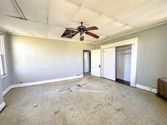 unfurnished bedroom with a drop ceiling, radiator heating unit, wooden walls, ceiling fan, and a closet