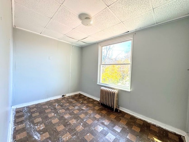 empty room featuring radiator heating unit and a drop ceiling