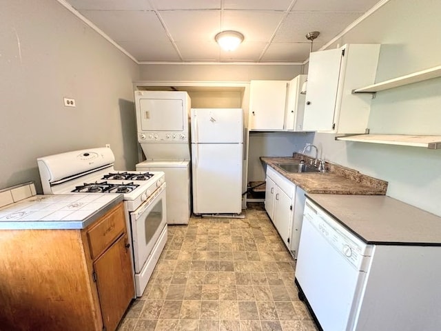 kitchen featuring sink, hanging light fixtures, white appliances, stacked washing maching and dryer, and white cabinets