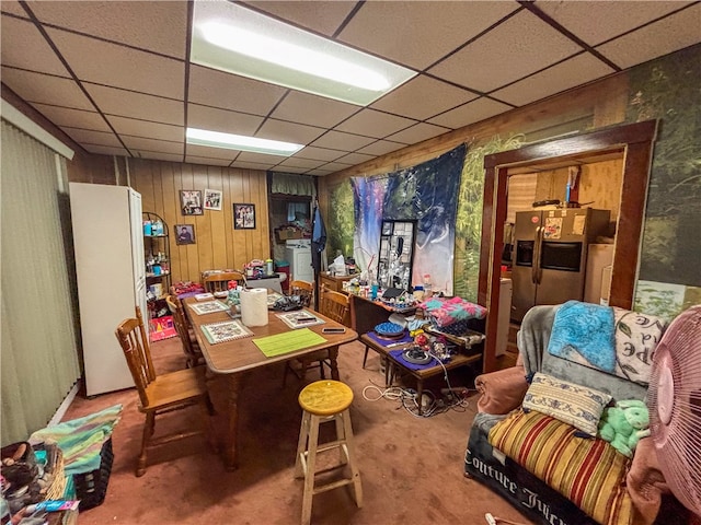 carpeted home office featuring wood walls and a drop ceiling