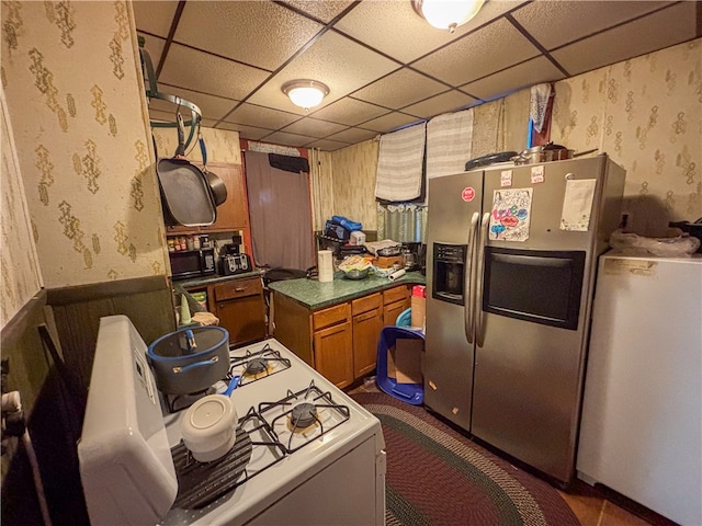 kitchen featuring gas range gas stove, refrigerator, a drop ceiling, and stainless steel fridge