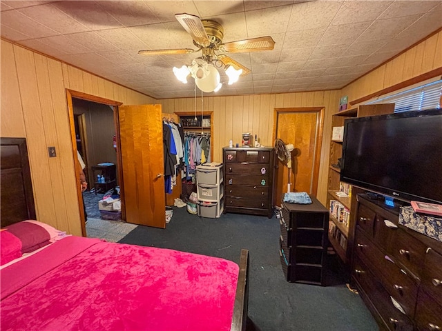 bedroom with wood walls, ceiling fan, dark carpet, and a closet