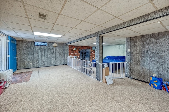 basement with a drop ceiling and wooden walls