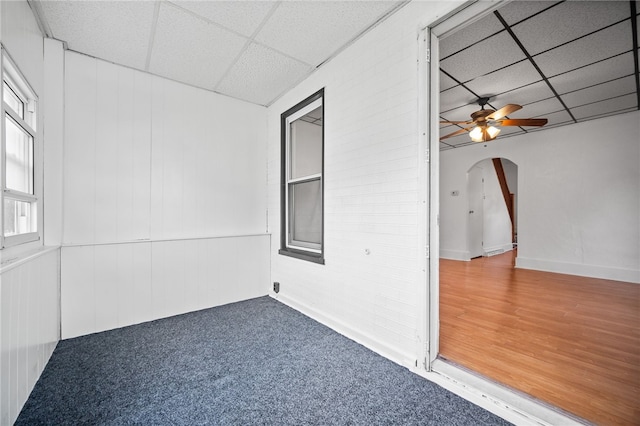 spare room featuring wood walls, a drop ceiling, hardwood / wood-style floors, and ceiling fan