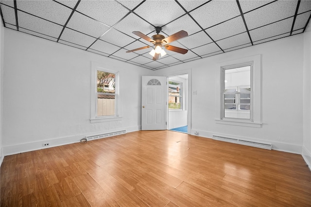 empty room featuring a paneled ceiling, hardwood / wood-style floors, ceiling fan, and a baseboard heating unit