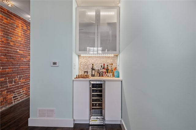 bar featuring dark wood-type flooring, brick wall, and wine cooler