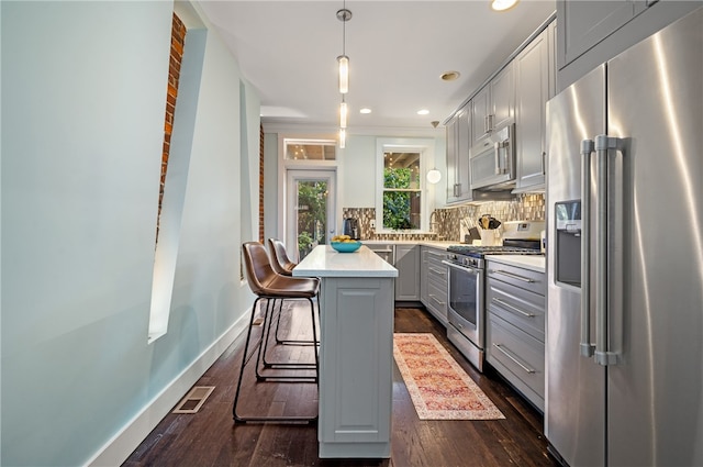 kitchen featuring stainless steel appliances, dark hardwood / wood-style flooring, a center island, a kitchen breakfast bar, and pendant lighting