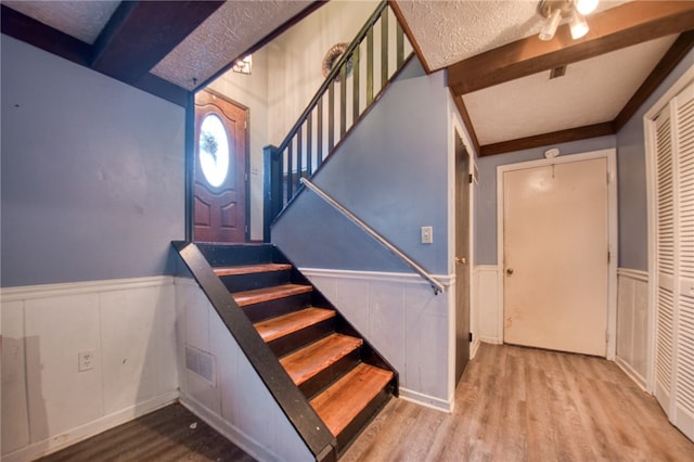 stairs with hardwood / wood-style floors, a textured ceiling, and beam ceiling