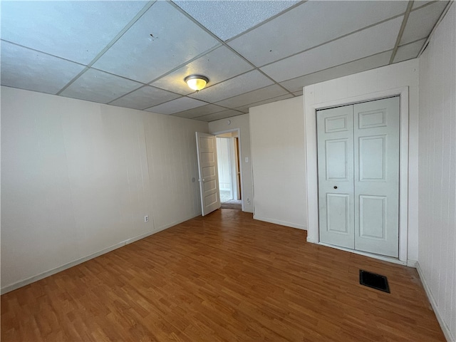 unfurnished bedroom with a closet, a paneled ceiling, and wood-type flooring