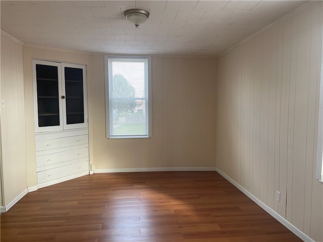 spare room featuring dark hardwood / wood-style flooring, wood walls, and ornamental molding