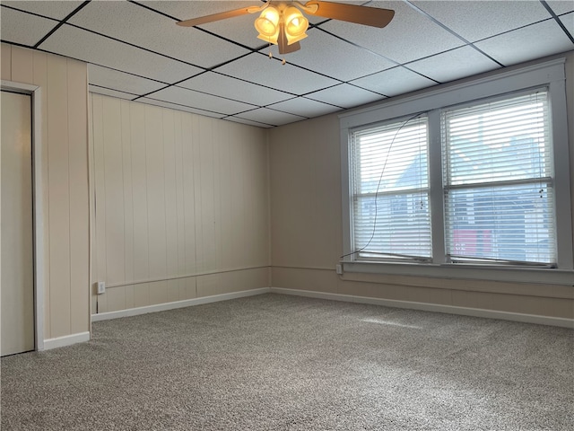 carpeted spare room featuring a paneled ceiling, wooden walls, and ceiling fan