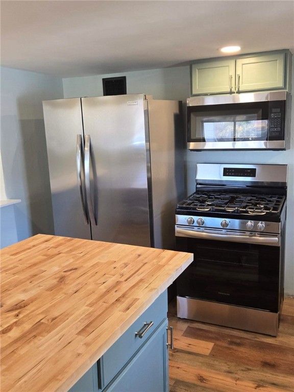 kitchen with hardwood / wood-style flooring, green cabinetry, butcher block countertops, and appliances with stainless steel finishes