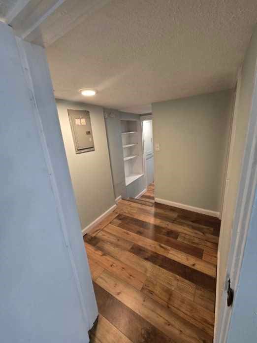 corridor featuring dark wood-type flooring, a textured ceiling, and electric panel