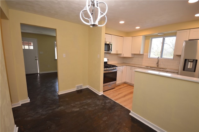 kitchen featuring pendant lighting, decorative backsplash, sink, white cabinetry, and appliances with stainless steel finishes