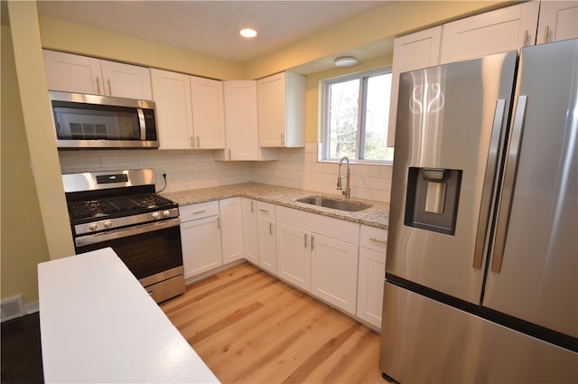 kitchen featuring stainless steel appliances, white cabinets, decorative backsplash, sink, and light wood-type flooring