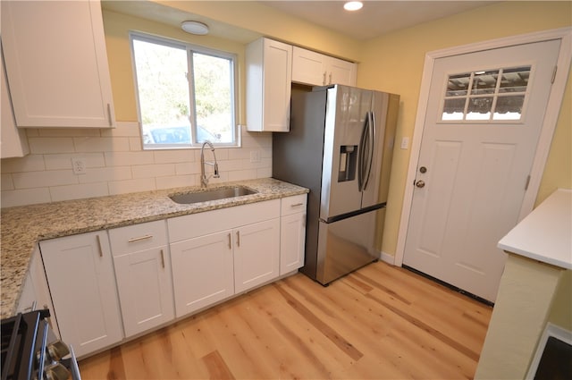 kitchen with sink, stainless steel fridge with ice dispenser, light stone countertops, white cabinetry, and light wood-type flooring