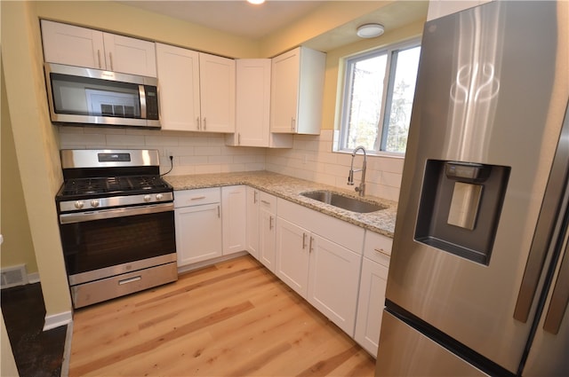 kitchen with stainless steel appliances, sink, light stone counters, tasteful backsplash, and white cabinets