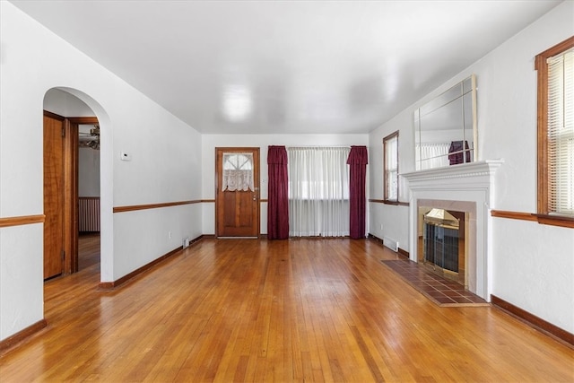 unfurnished living room featuring a tiled fireplace, plenty of natural light, light hardwood / wood-style floors, and radiator