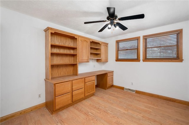 unfurnished office featuring ceiling fan, built in desk, and light hardwood / wood-style flooring