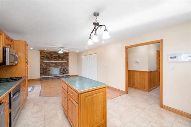 kitchen with a kitchen island, decorative light fixtures, stainless steel appliances, wooden walls, and ceiling fan