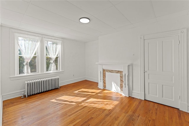 unfurnished living room with hardwood / wood-style floors, a fireplace, and radiator heating unit