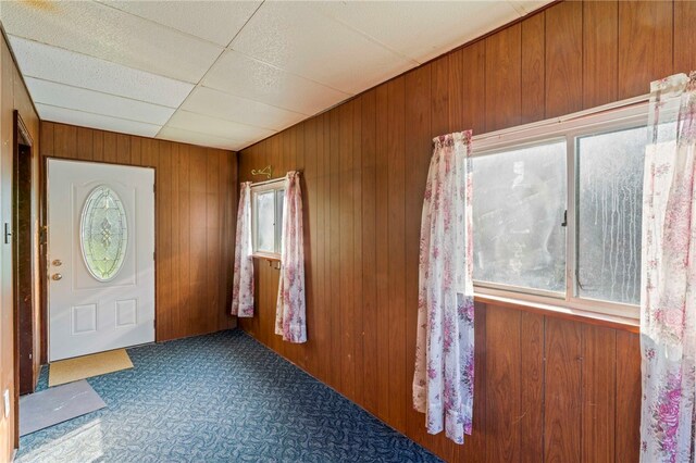 foyer featuring a drop ceiling, carpet, and wooden walls