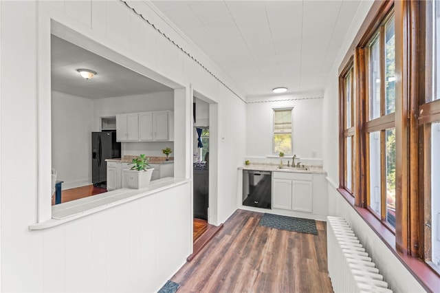 kitchen with black appliances, a wealth of natural light, radiator heating unit, and white cabinets