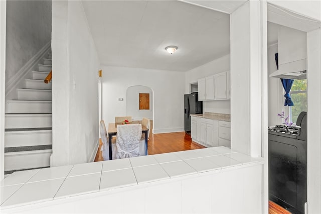 kitchen with light hardwood / wood-style floors, tile countertops, white cabinets, black fridge with ice dispenser, and washer / dryer