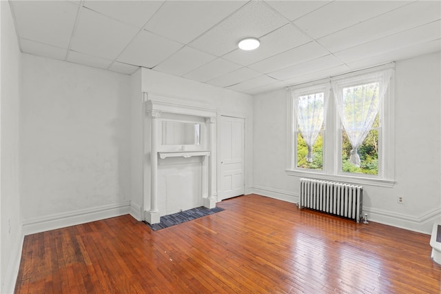 unfurnished living room featuring a drop ceiling, radiator heating unit, and wood-type flooring