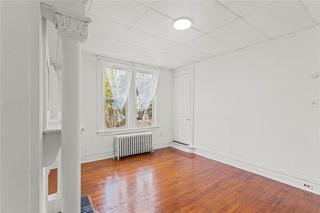 spare room with a paneled ceiling, wood-type flooring, and radiator