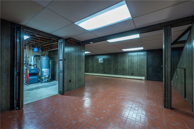 basement featuring gas water heater, a baseboard radiator, wooden walls, and a drop ceiling