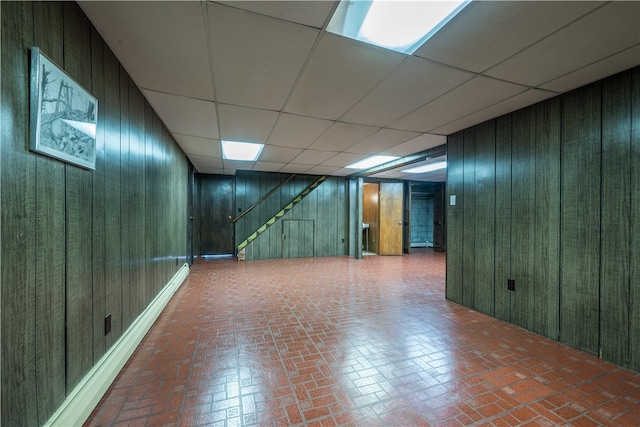 basement with baseboard heating, wooden walls, and a drop ceiling